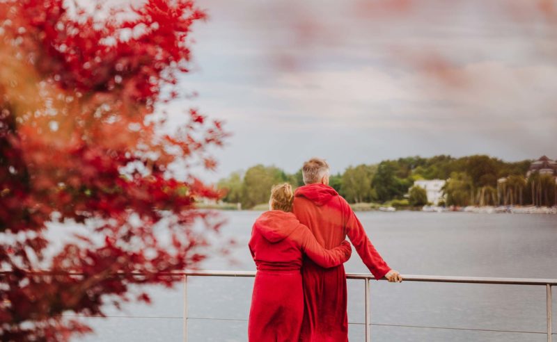 Paar in roten Bademänteln genießt Ausblick über den herbstlichen Ruppiner See