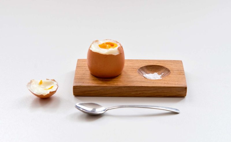 Gekochtes Ei auf einem Holzbrett mit Salz und Löffel daneben