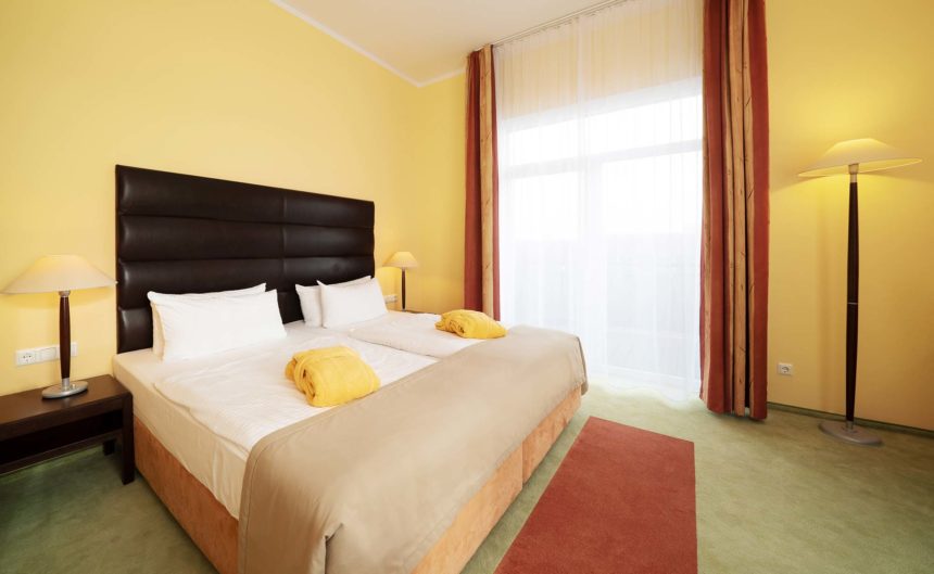 Doppelbett mit gelben Bademantel darauf im Superior Zimmer Hotel Neuruppin