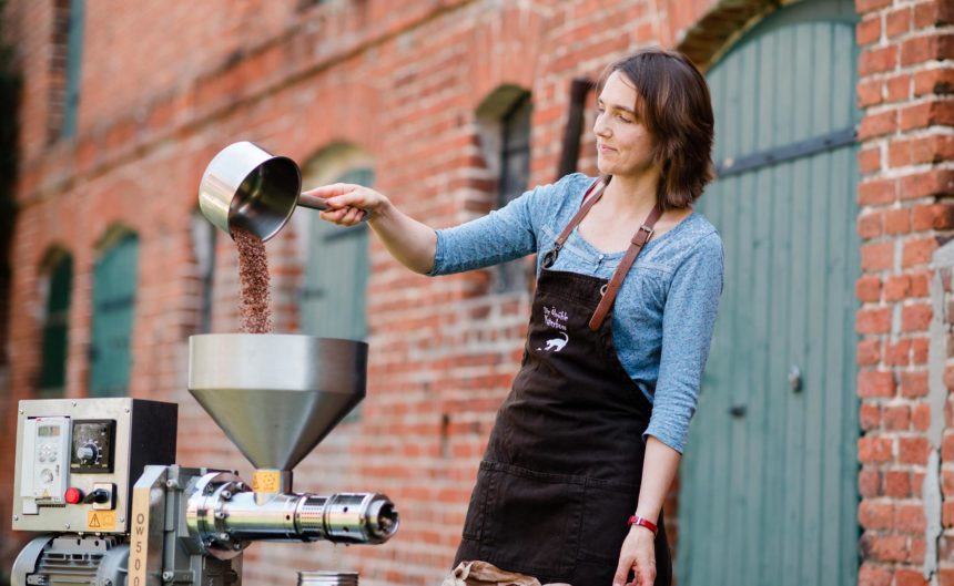 Frau mit Schürze schüttet Kaffeebohnen in einen Trichter zum zermahlen