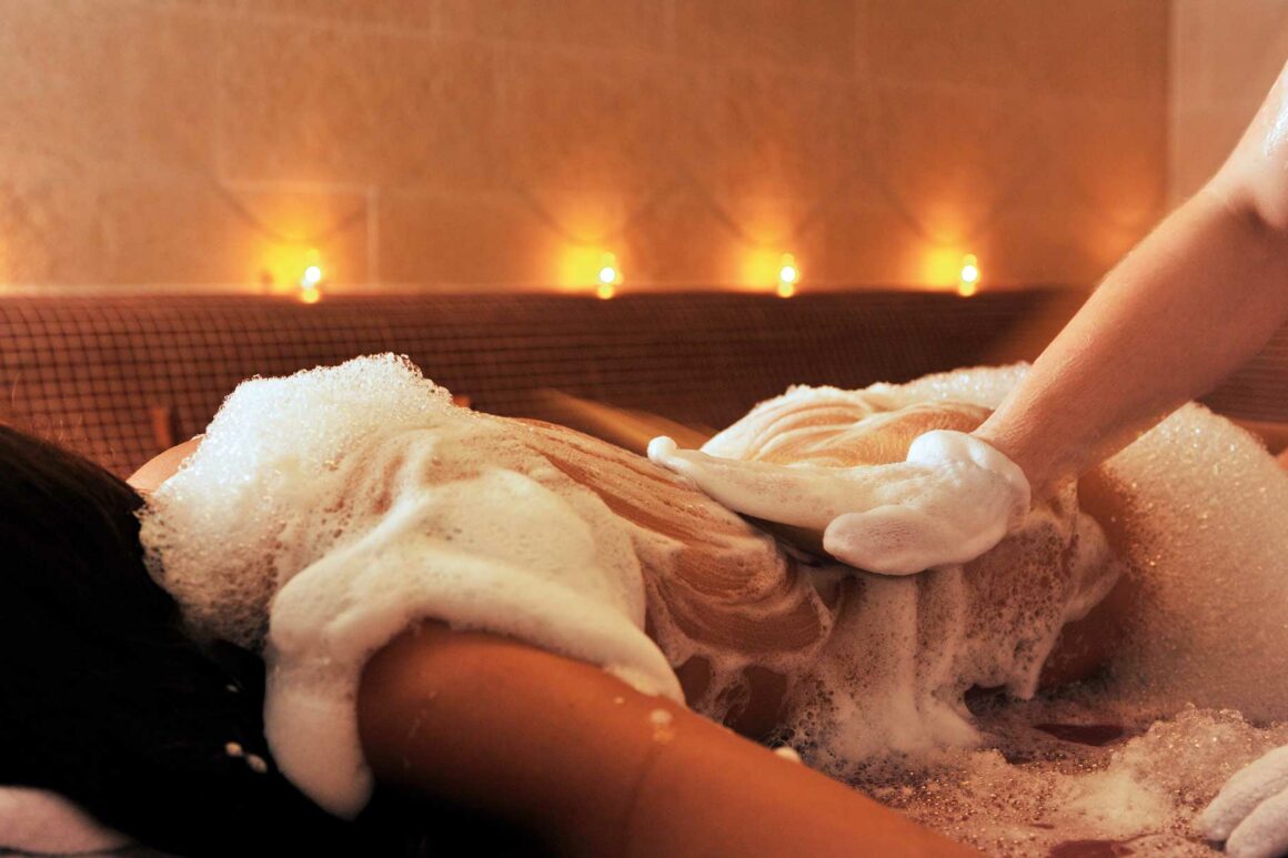Frau genießt entspannende Massage mit Peeling Handschuh bei stimmungsvoller Beleuchtung