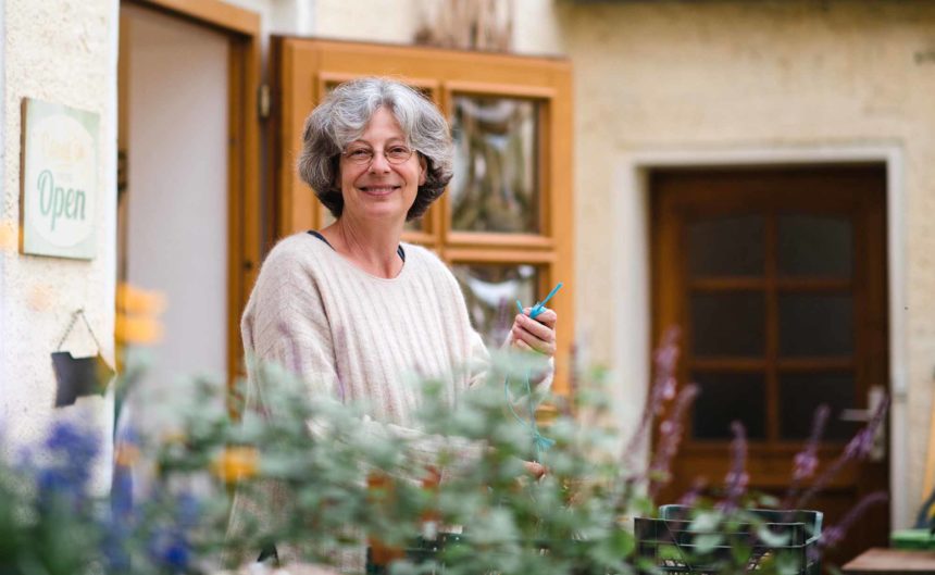 Frau bindet Tomatenpflanzen und lächelt in die Kamera