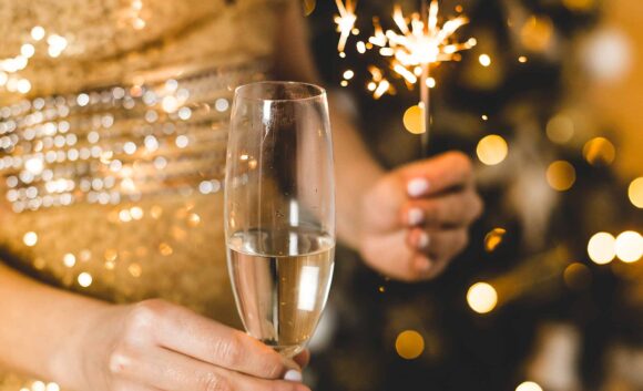 Ein Glas Sekt und Wunderkerze vor gold glitzerndem Hintergrund