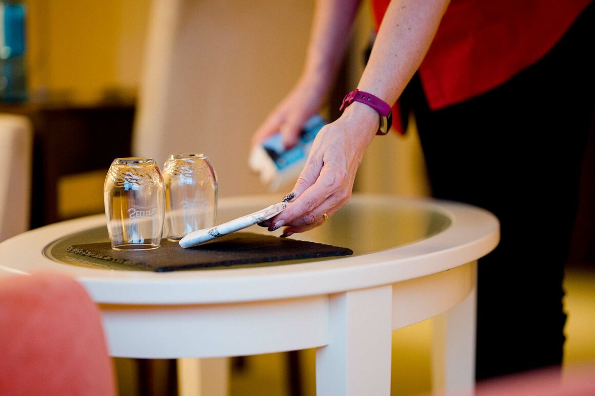 Nahaufnahme einer Person, die in einem Hotelzimmer einen Beistelltisch mit zwei Gläsern vorbereitet.