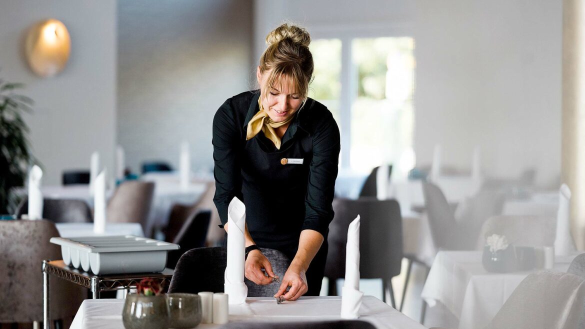 Mitarbeiterin des Resort Mark Brandenburg deckt einen Tisch in einem Restaurant für Gäste.