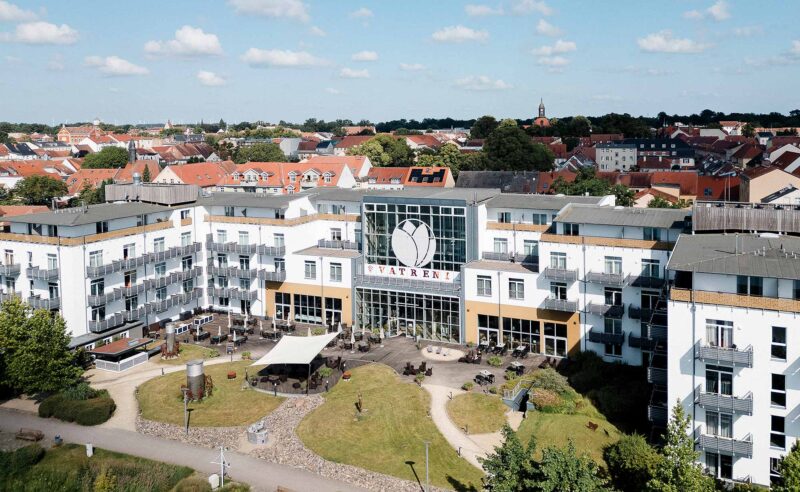 Frontale Luftaufnahme des Resort Mark Brandenburg mit Vatreni-Schriftzug, Terrasse und begrüntem Vorplatz vor dem Stadtpanorama Neuruppins
