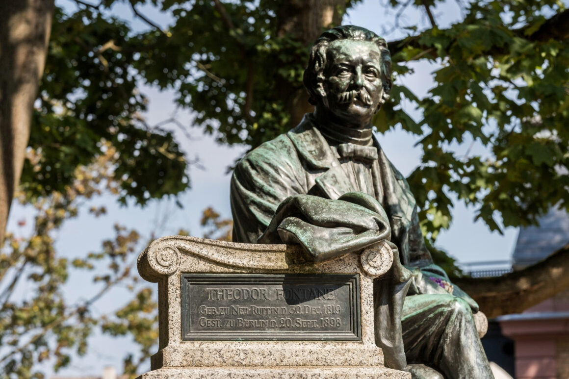 Bronzestatue von Theodor Fontane auf einem Steinsockel mit Inschrift: Geb. zu Neu-Ruppin d. 30. Dec. 1819, Gest. zu Berlin d. 20. Sept. 1898
