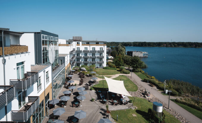 Luftaufnahme des Resort Mark Brandenburg mit Außenterrasse, Sonnenschirmen und Blick auf den Ruppiner See