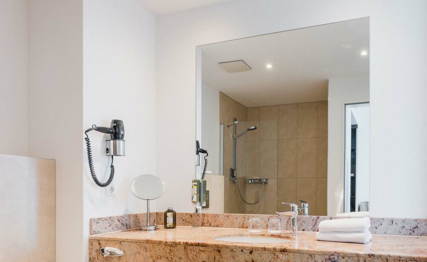 Blick auf einen Spiegel eines Badezimmer über einem Waschbecken, in dem sich die Dusche spiegelt.