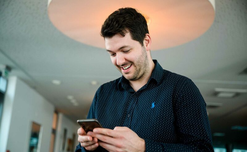 Mann hält ein Handy in den Händen und lacht.