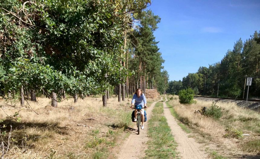 Frau radelt einen Weg entlang trockener Sträucher durch die Region Neuruppin