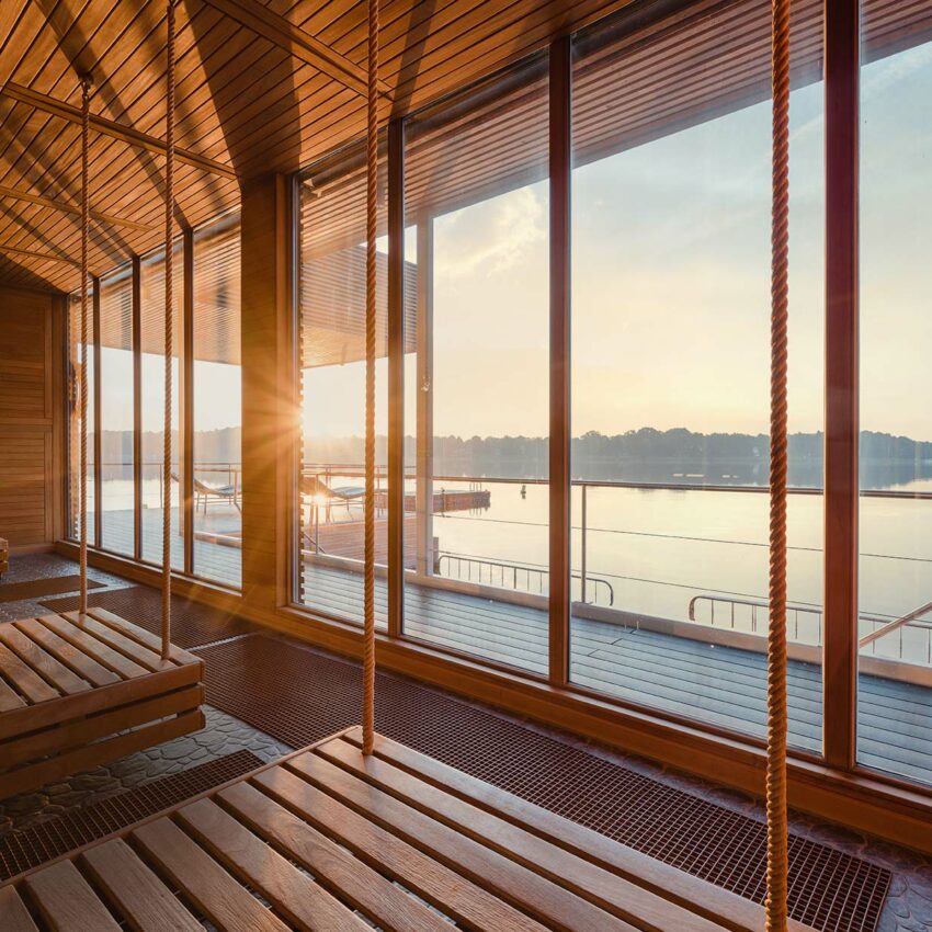 Blick von hängenden Holzliegen durch eine große Fensterfront auf den Ruppiner See hinaus.