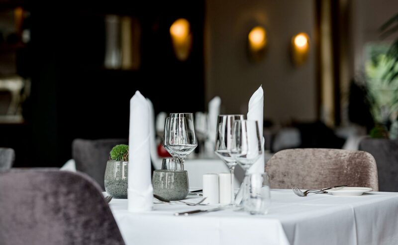 Gedeckter Tisch im Vordergrund eines hellen Restaurants mit weiteren Tischen im Hintergrund.