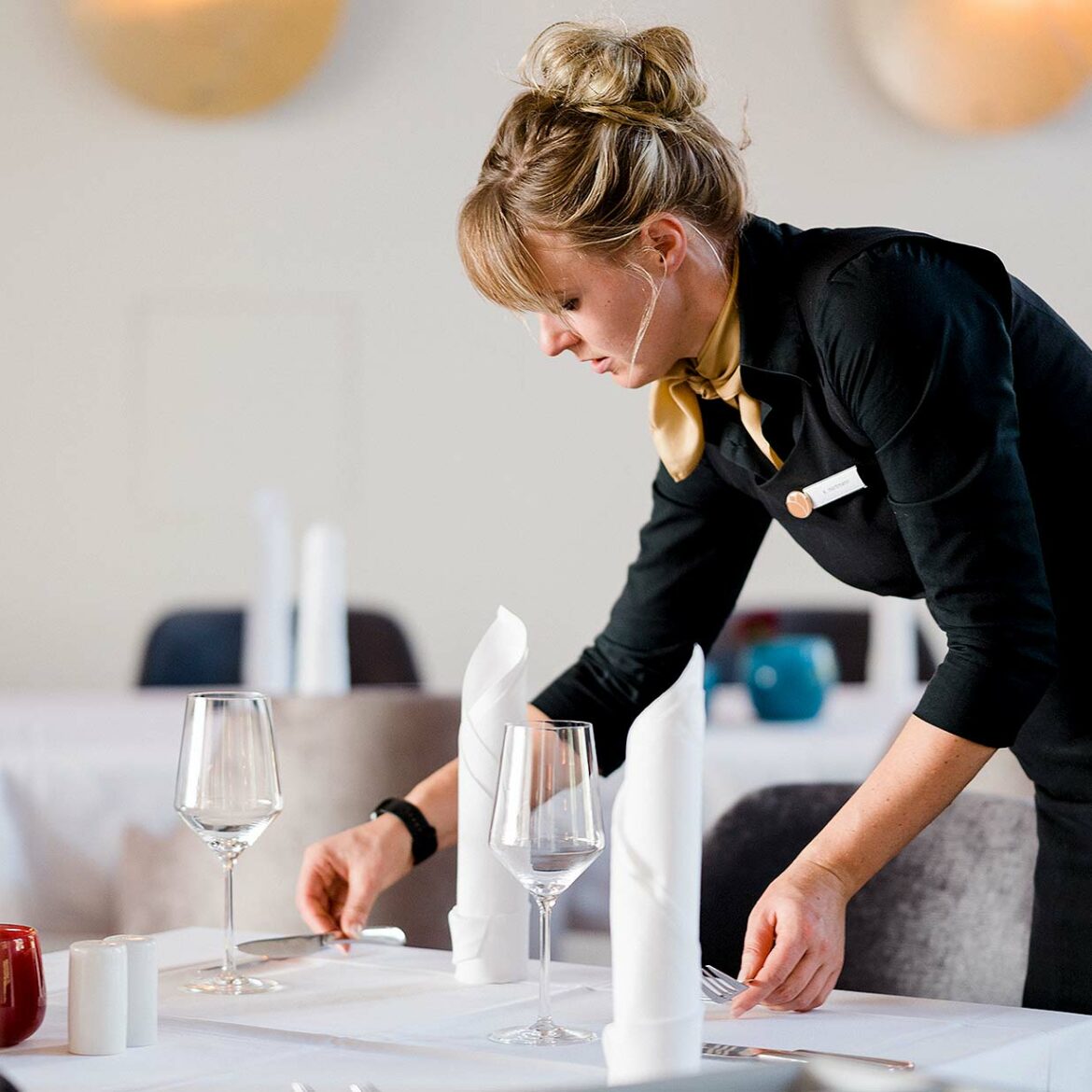 Eine Servicemitarbeiterin des Resort Mark Brandenburg deckt konzentriert einen Tisch.