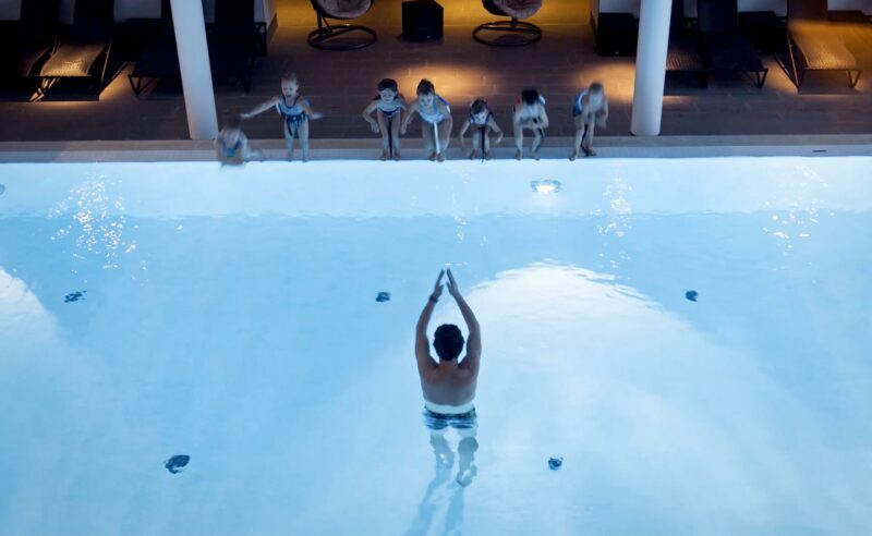 Ein Mann im Wasser gibt einen Schwimmkurs in der Fontane Therme für Kinder, die am Beckenrand stehen.
