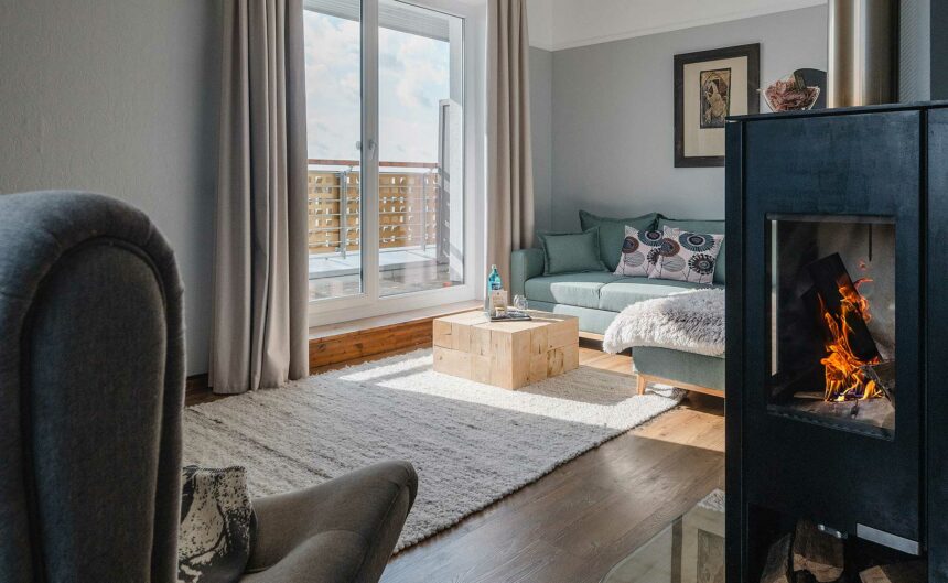 Lichtdurchflutetes Suite mit großer Couch, Sessel sowie brennendem Kamin.